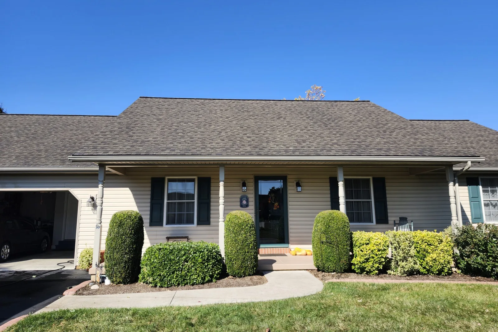 Same porch-front house after SoyFuze soy oil roof treatment, with darker, more uniform shingles