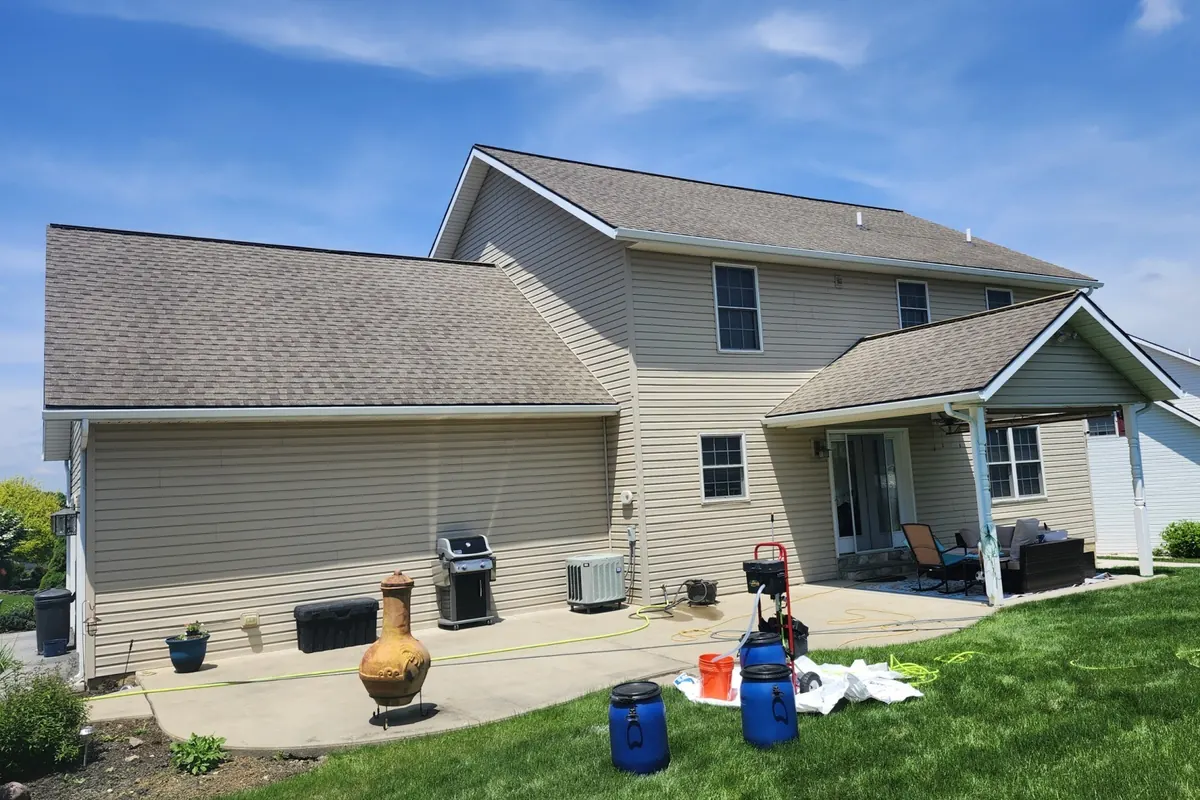 Washed-out dry light gray asphalt shingle roof on a beige two-story house before SoyFuze treatment